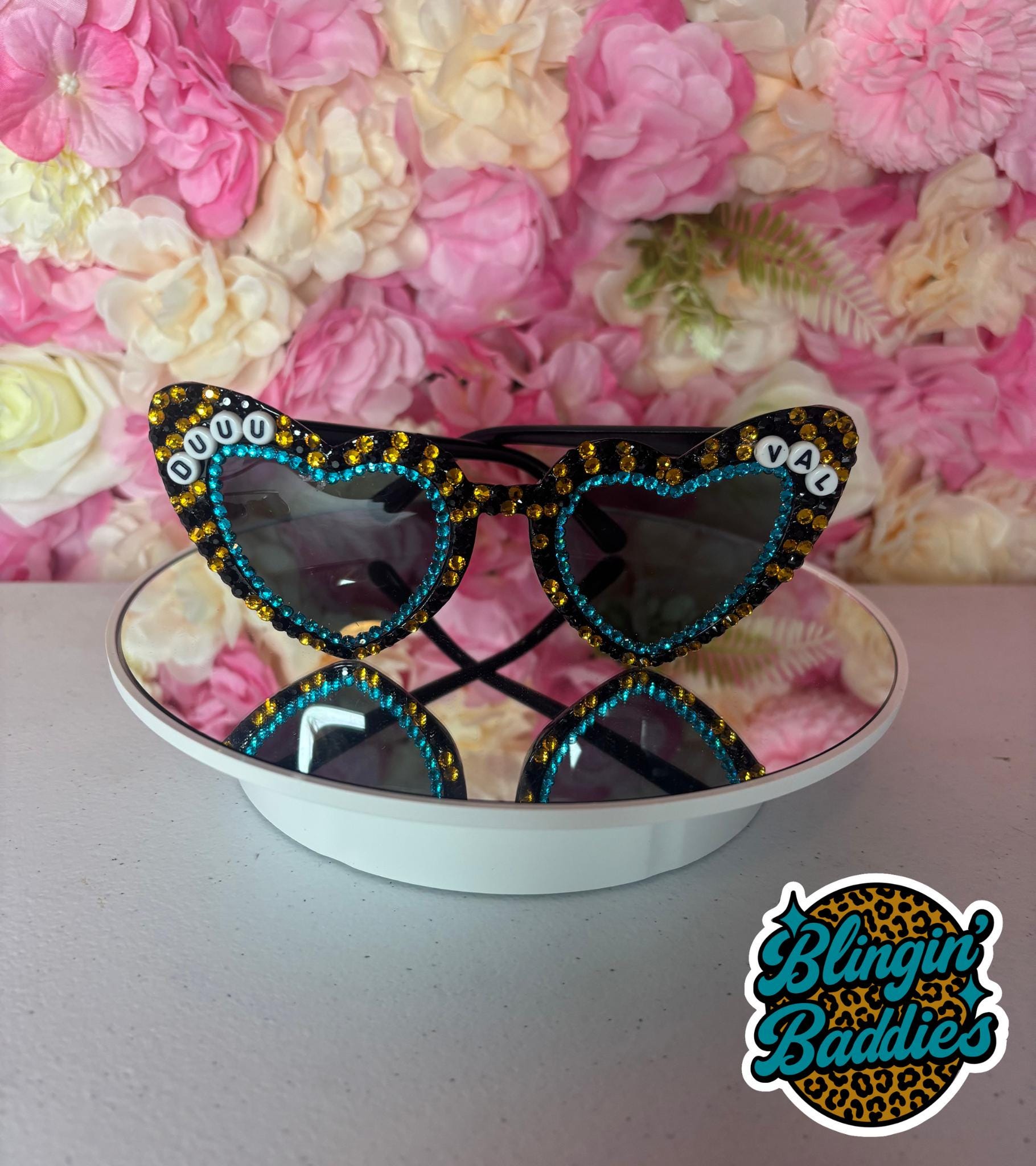 Custom GAMEDAY rhinestone heart sunglasses with teal and gold bling and DUUUVAL letter beads on floral backdrop