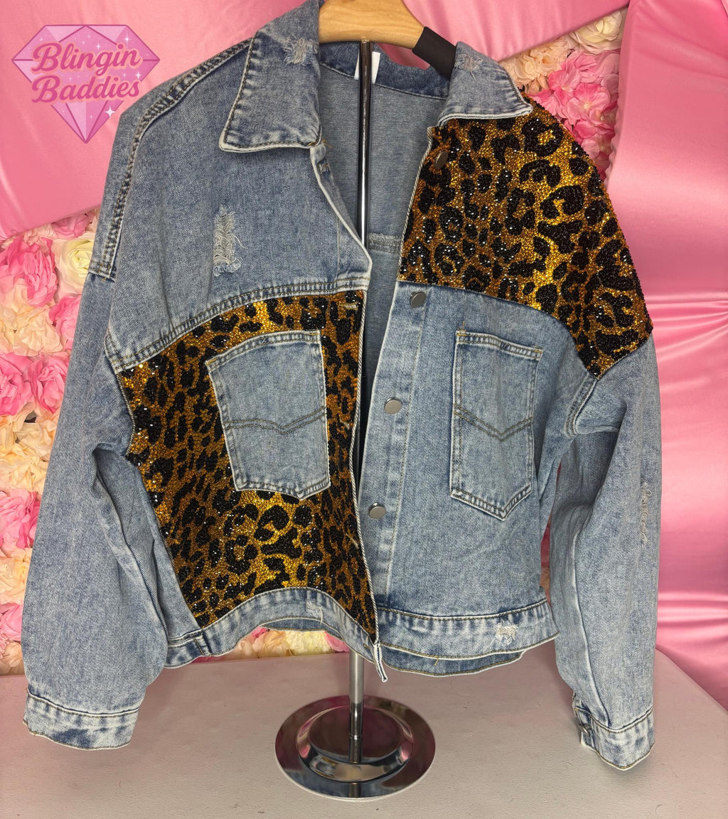 Full front view of leopard rhinestone denim jacket on mannequin against pink floral backdrop